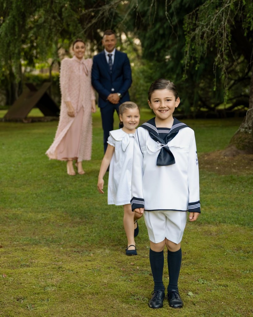 Contratar las fotografías de comunión con tiempo: niño de marinero con su hermana y sus padres en un jardín de Gijón