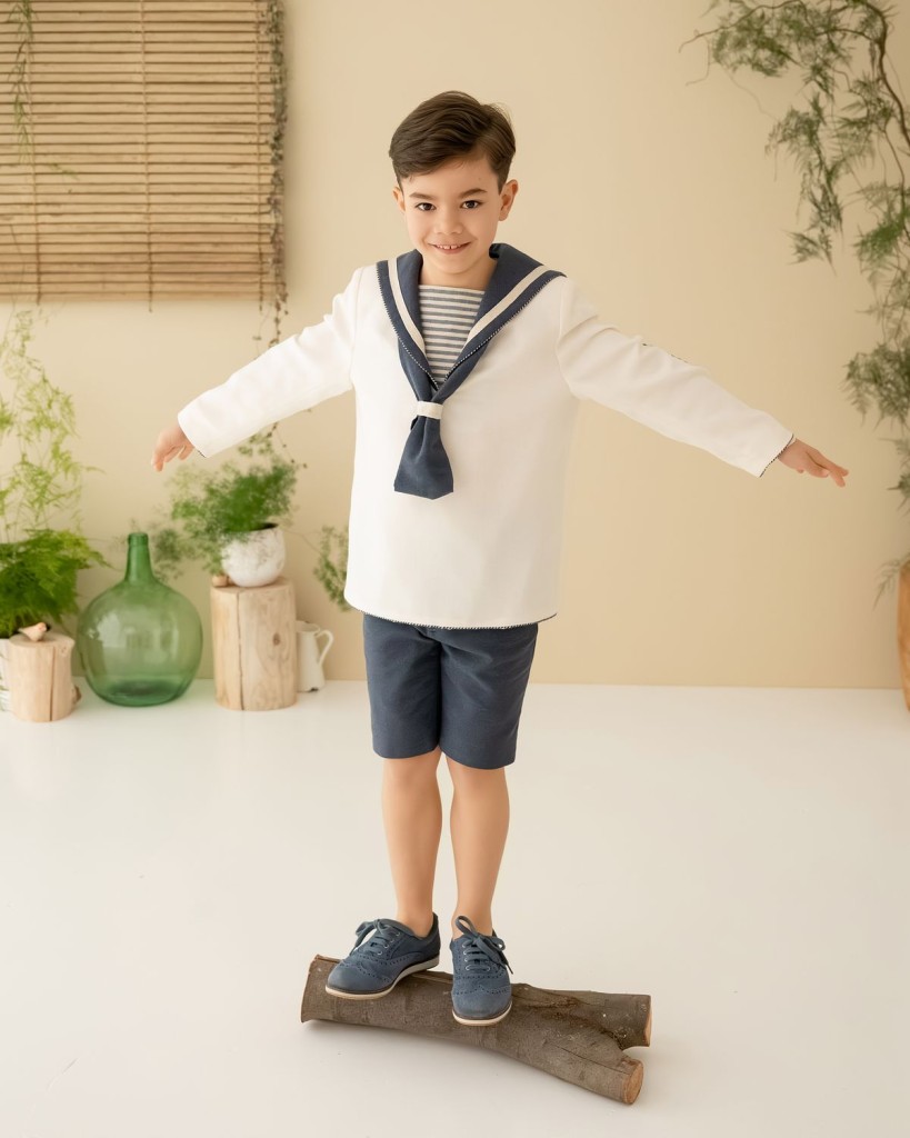 Fotografía de comunión en Asturias: niño con traje de marinero en equilibrio sobre un tronco en el estudio