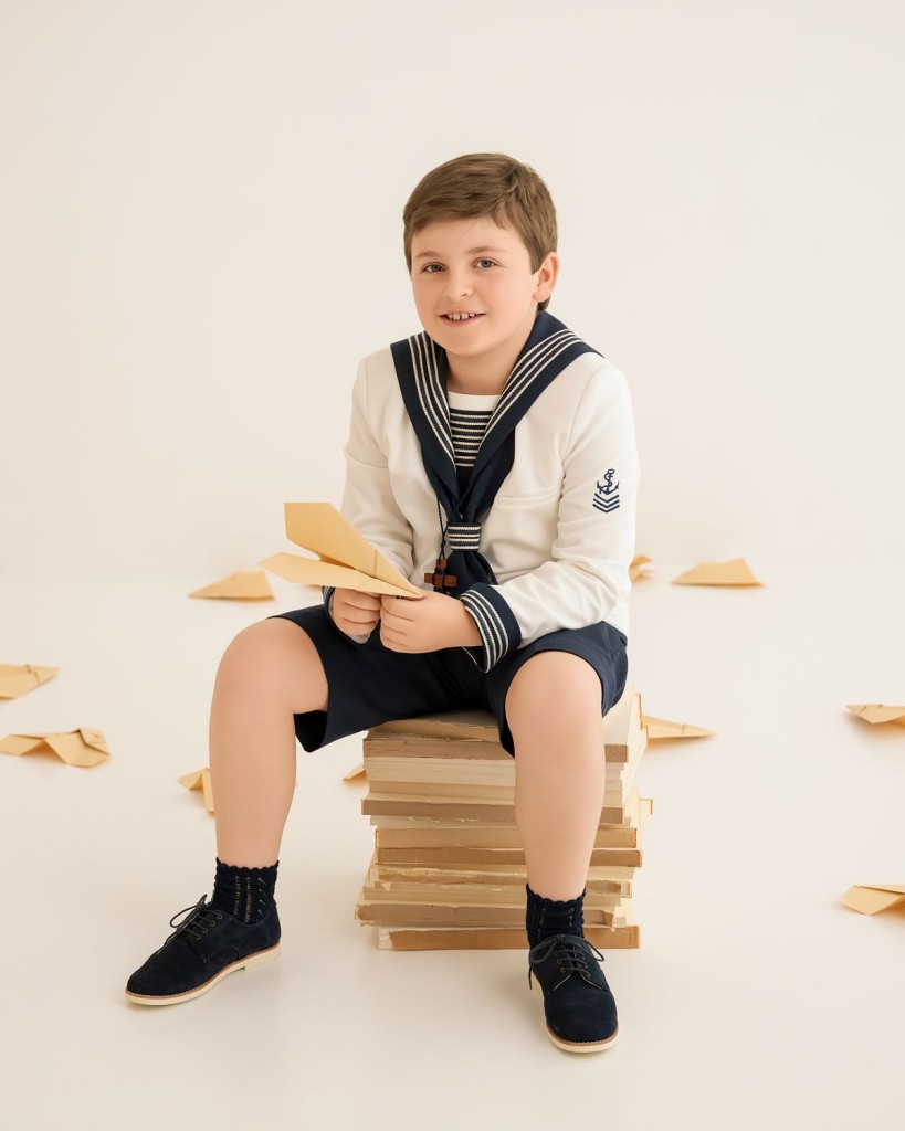 Fotógrafo de comunión en Gijón: niño de marinero sentado en libros con aviones de papel