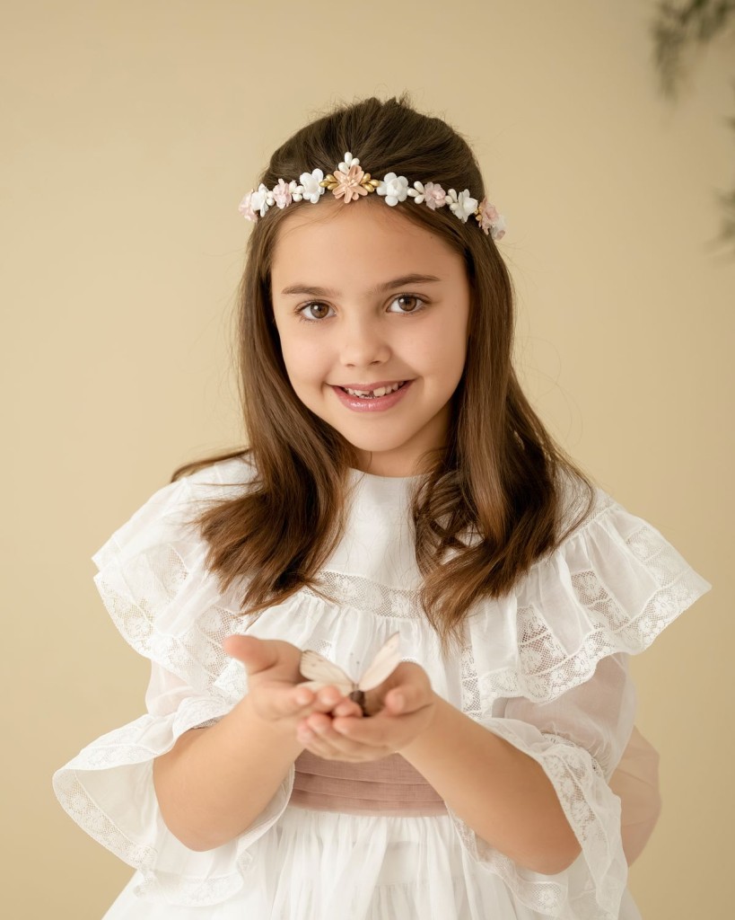 Fotos de comunión en Gijón: niña sonriente con corona de flores sosteniendo una mariposa