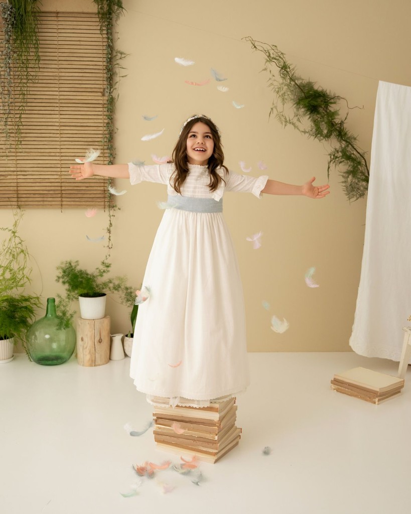 Reportaje de comunión en Gijón: niña con vestido de comunión rodeada de plumas en el estudio